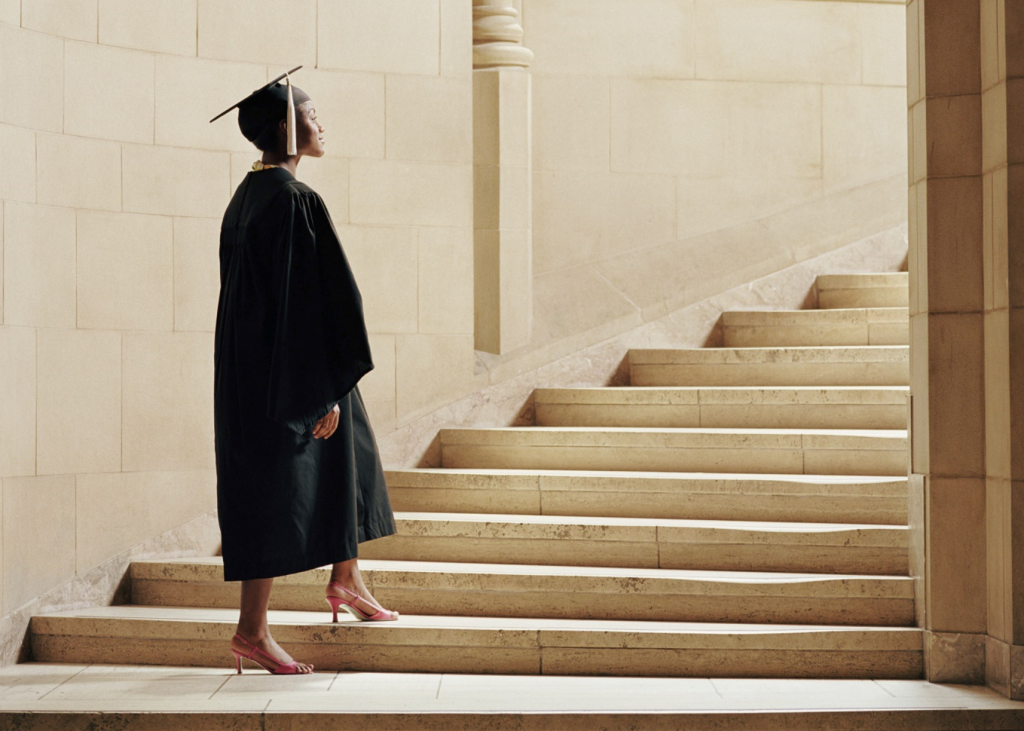 female student in cap and gown looking up stairs